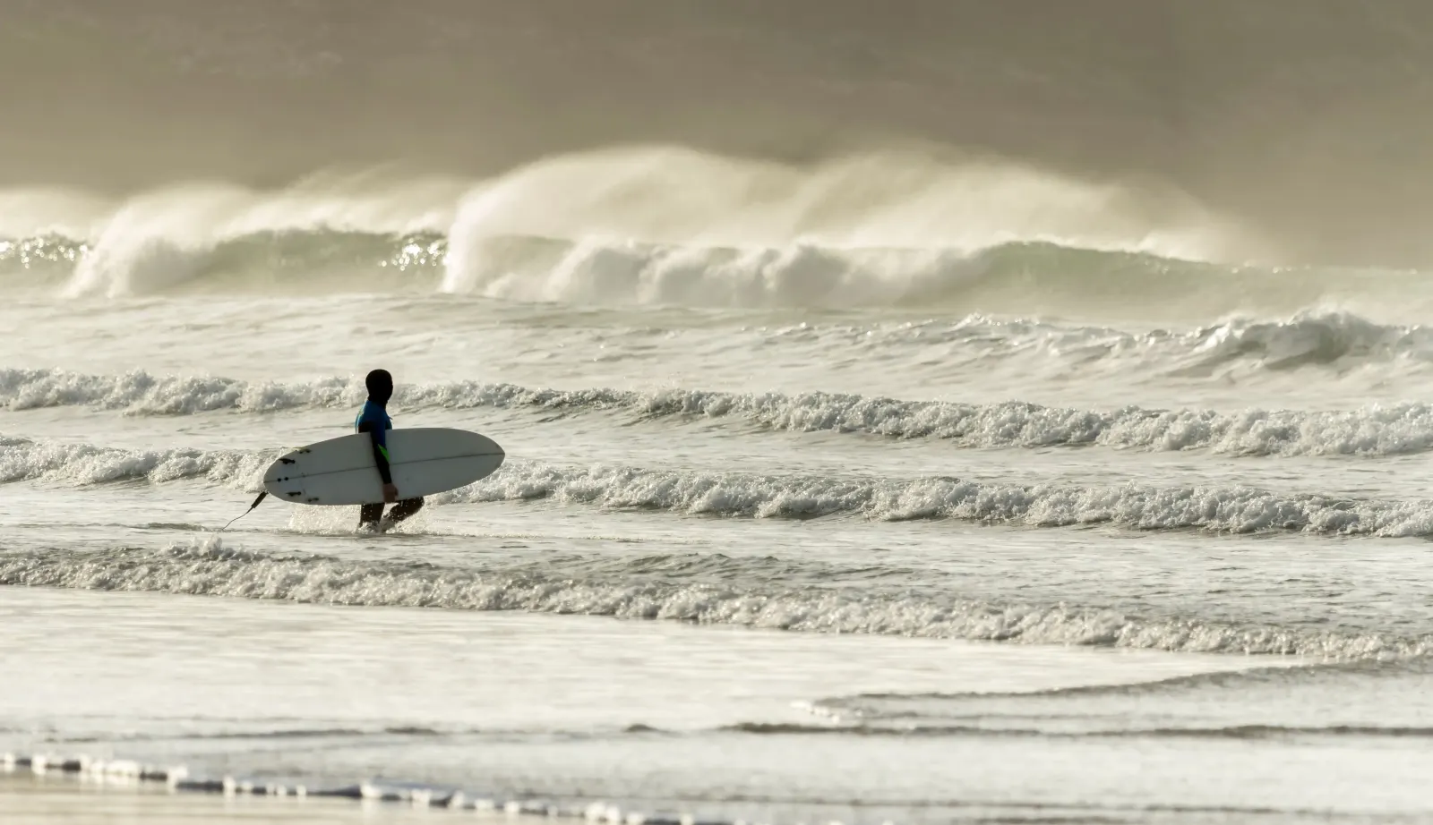Surfer approaches the waves at Fistral Beach, Newquay, Cornwall
